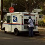 Mail carrier standing behind a USPS truck on a suburban street