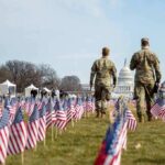 Two soldiers walk among American flags toward the U.S. Capitol
