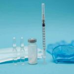 Syringe with vials, ampoules, mask, and gloves on blue background