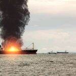 Cargo ship on fire with thick black smoke at sea