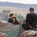 group of children and an older man sitting on a low wall outdoors