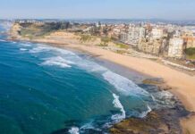 Aerial view of a coastal city beach with waves and rocky shoreline