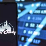 Walt Disney logo on smartphone with stock market chart background