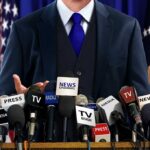 A speaker at a press conference with multiple microphones in front of them