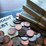 stacks of cash and coins next to a student debt note