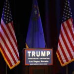 A Controversial Pardon Returns To The Spotlight Podium with campaign sign between American flags