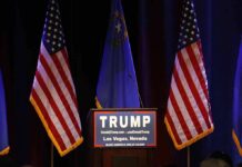 A Controversial Pardon Returns To The Spotlight Podium with campaign sign between American flags