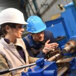 Two workers operating a metal lathe in a workshop
