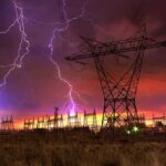 Lightning strikes illuminate a power station against a colorful sunset sky