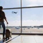 Traveler with suitcase watching plane through airport window