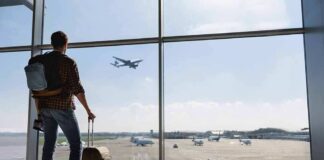 Traveler with suitcase watching plane through airport window