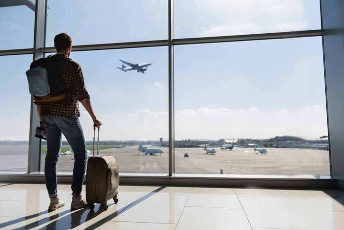 Traveler with suitcase watching plane through airport window