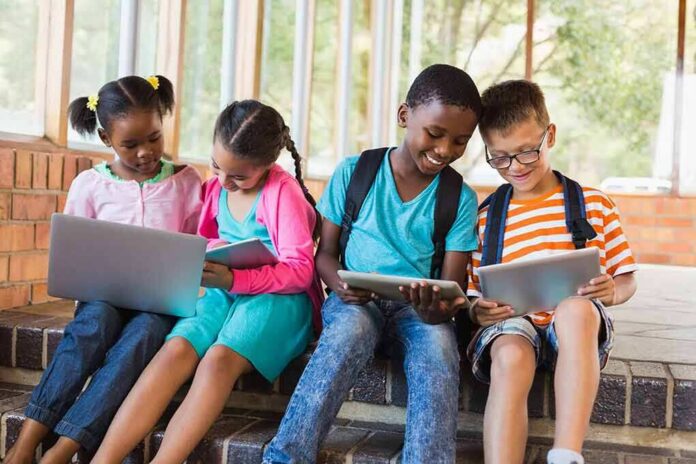 Children using laptops and tablets on school steps