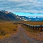 Pipeline crossing a broad valley with mountains under a cloudy sky