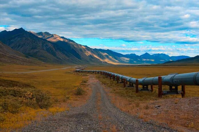 Pipeline crossing a broad valley with mountains under a cloudy sky