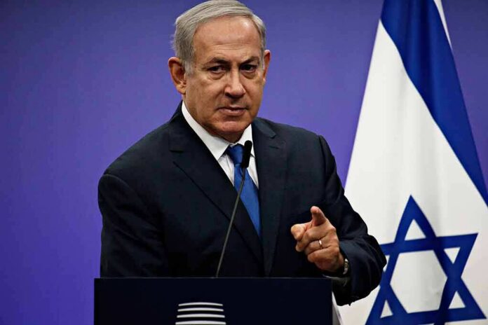 man in suit speaking at a podium with an Israeli flag