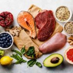Assorted healthy foods with salmon, beef, chicken, fruits, vegetables, nuts, and grains