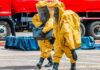 Hazmat workers in yellow suits carry equipment near a tanker truck