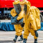 Hazmat workers in yellow suits carry equipment near a tanker truck