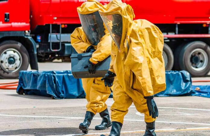 Hazmat workers in yellow suits carry equipment near a tanker truck