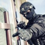 tactical officer in black gear reaching for a door handle