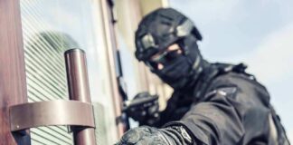 tactical officer in black gear reaching for a door handle