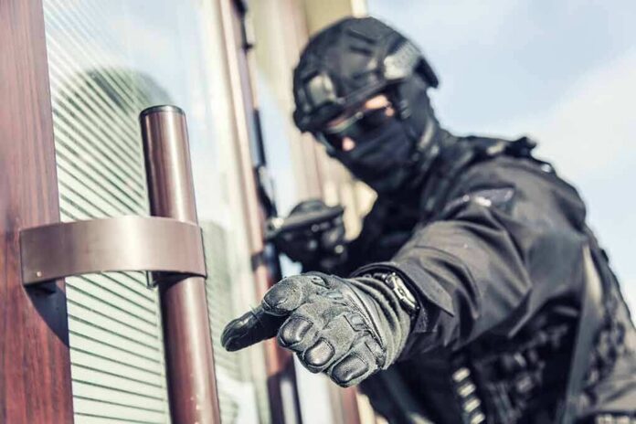 shutterstock_1391041319 tactical officer in black gear reaching for a door handle