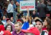 Child holding a 'Latinos for Trump' sign at a crowded rally
