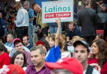 Child holding a 'Latinos for Trump' sign at a crowded rally