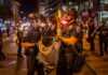 15-Year-Old Arrested After Woman’s Face Burned Police officers detain a protester at night on a city street