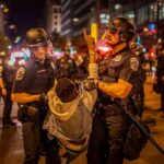Police officers detain a protester at night on a city street