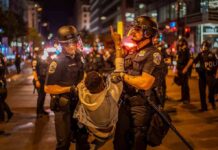 Police officers detain a protester at night on a city street