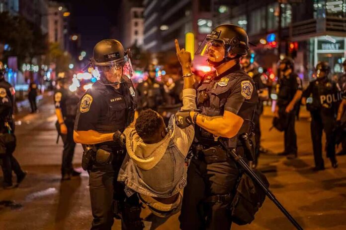 Police officers detain a protester at night on a city street