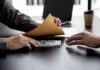 Hands exchanging cash in an envelope at a desk