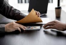Hands exchanging cash in an envelope at a desk