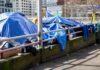 Tents covered with blue tarps along a city sidewalk