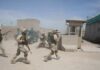 Soldiers in desert uniforms run past a checkpoint amid dust