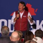 man speaking on stage at a rally