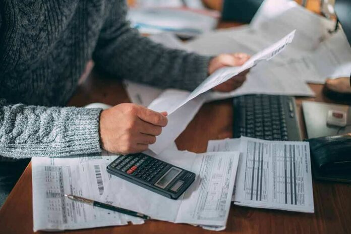 Person reviewing bills with calculator at cluttered desk